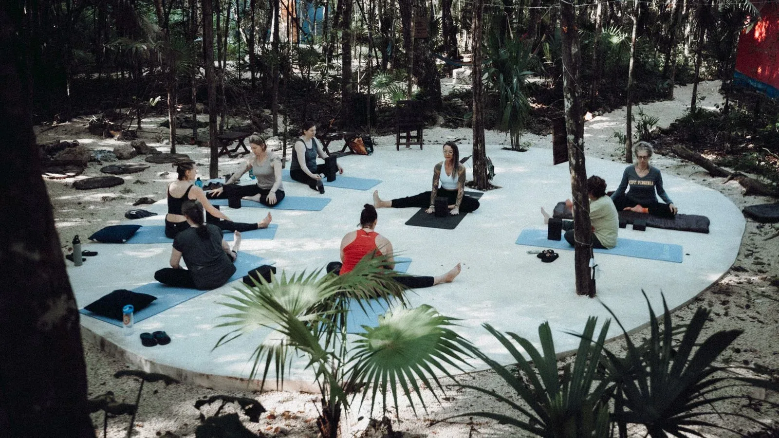Yoga class on the open-air platform at Lunita Jungle Retreat, women seated on blue mats in dappled light.
