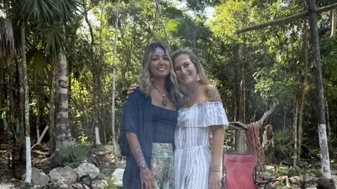 Karina with her friend and guide Nina, arm in arm on a white gravel path in the Mexican jungle