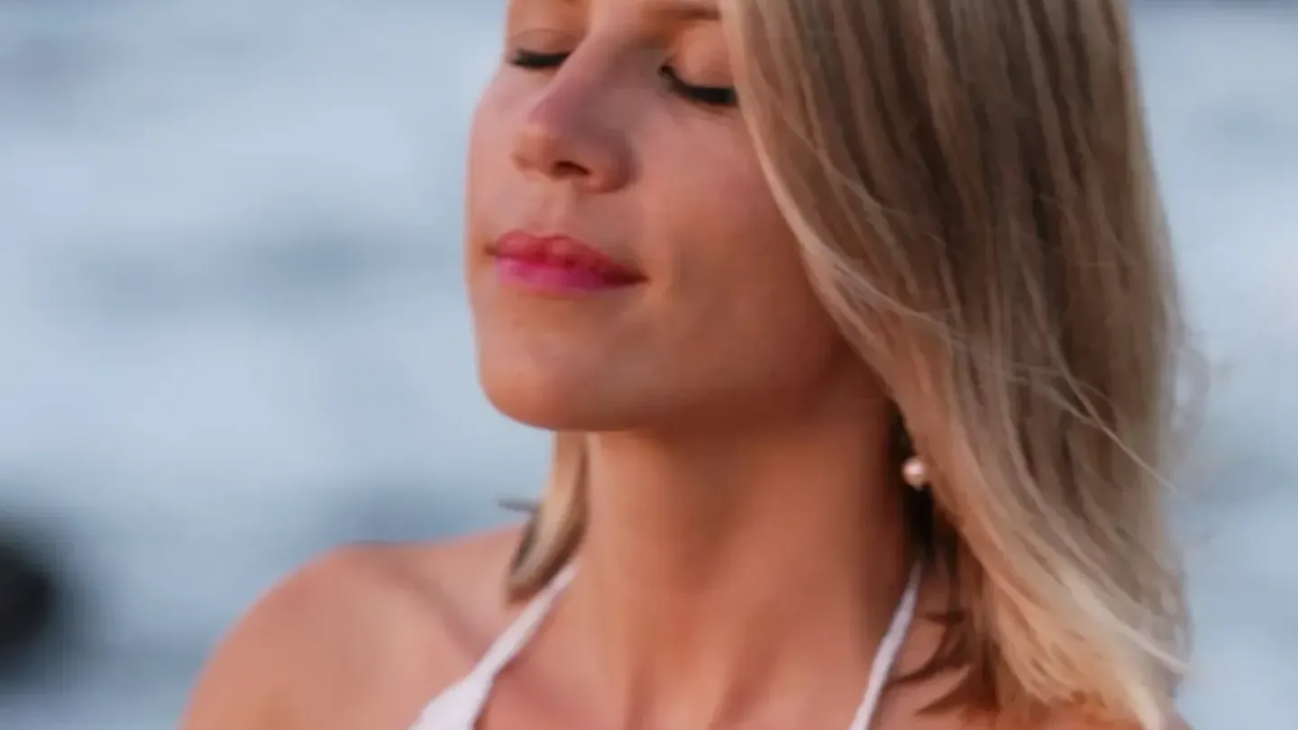 Alexandra Zuber, co-founder of RECLAIM, eyes closed with her hands on her chest by the sea