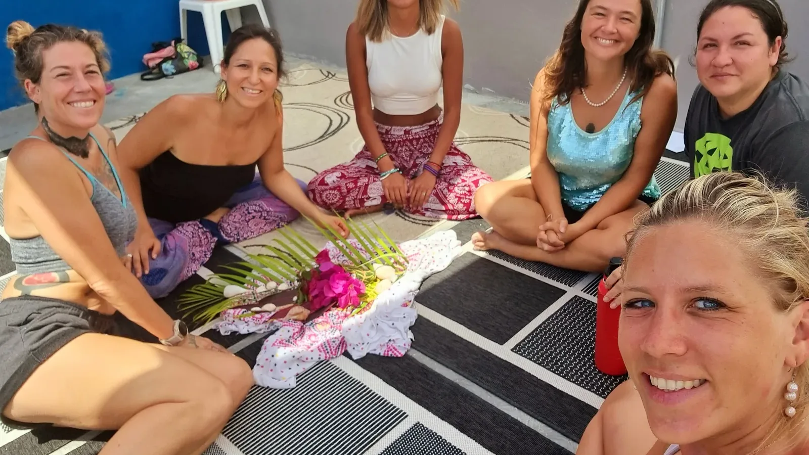 Six women smiling around a small altar of palm fronds and pink flowers at a women's circle in Puerto Morelos, 2023