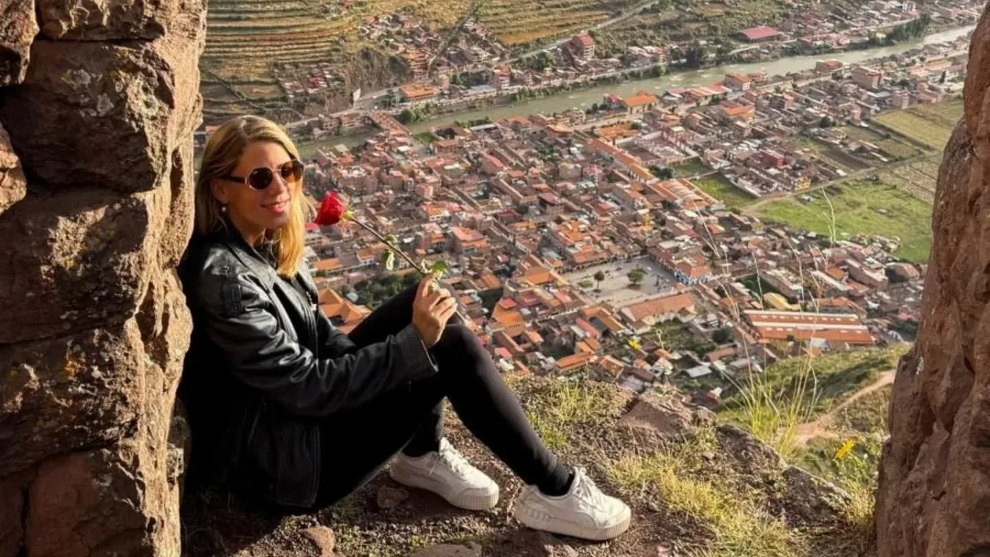 Alexandra sitting against an Inca stone wall with a red rose, the Sacred Valley of Peru below, 2025