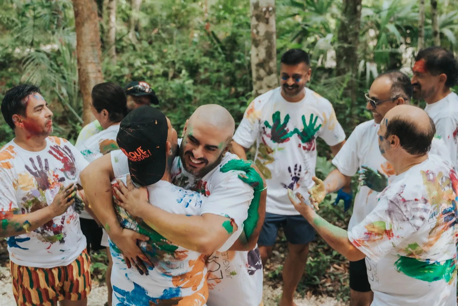 Eight people wearing white t-shirts painted with colorful handprints gather in a dense jungle, Lunita Jungle Retreat