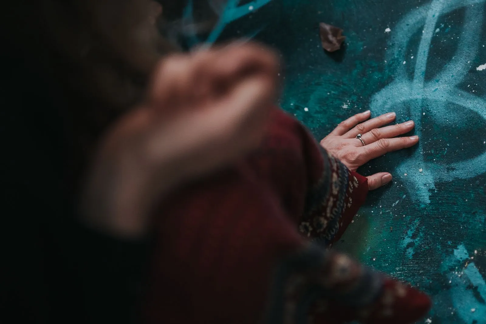 A hand with a silver ring presses against rough teal-painted concrete or stone wall, Lunita Jungle Retreat