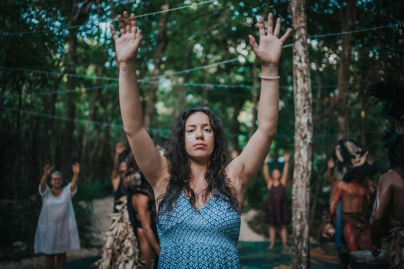 A woman in a teal patterned dress stands with arms raised in a jungle clearing, Lunita Jungle Retreat