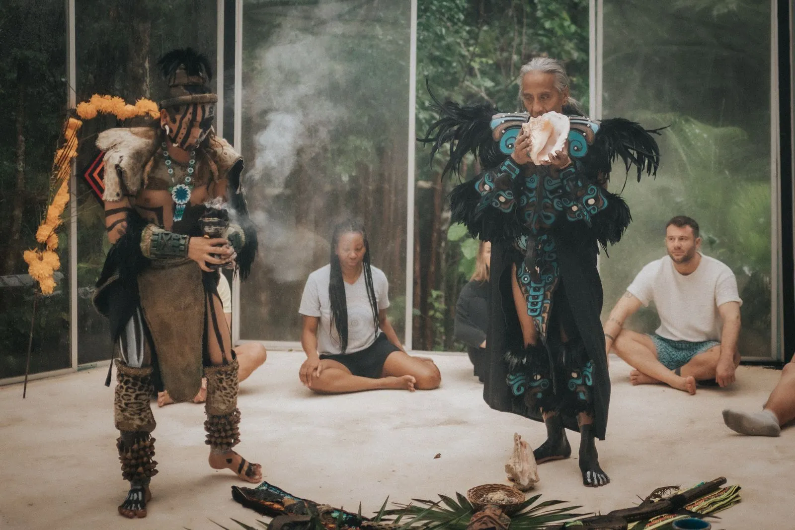 Two performers in elaborate feathered and beaded indigenous ceremonial attire move across a concrete, Lunita Jungle Retreat