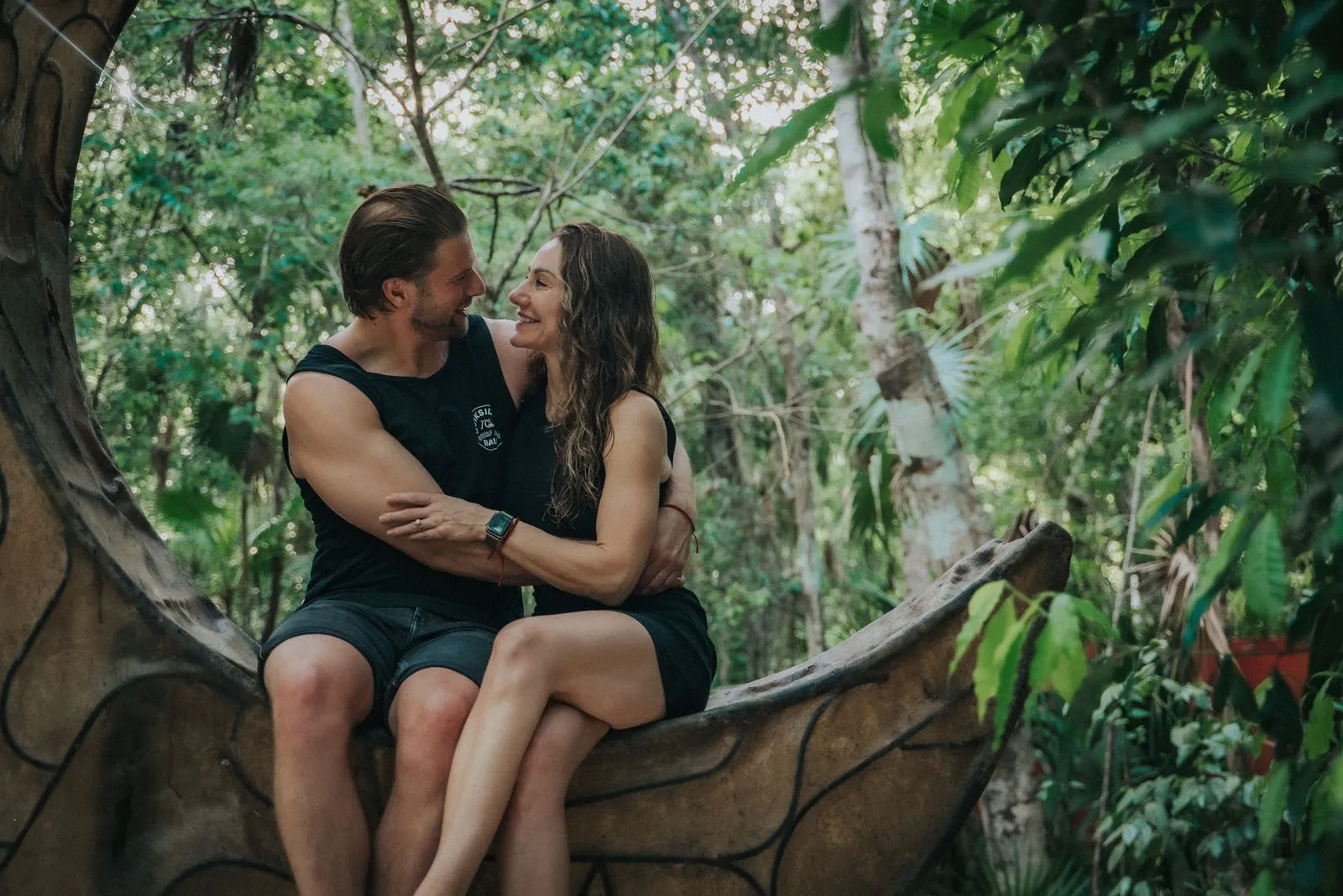 Two people sit on a curved tree trunk in dappled jungle light, Lunita Jungle Retreat