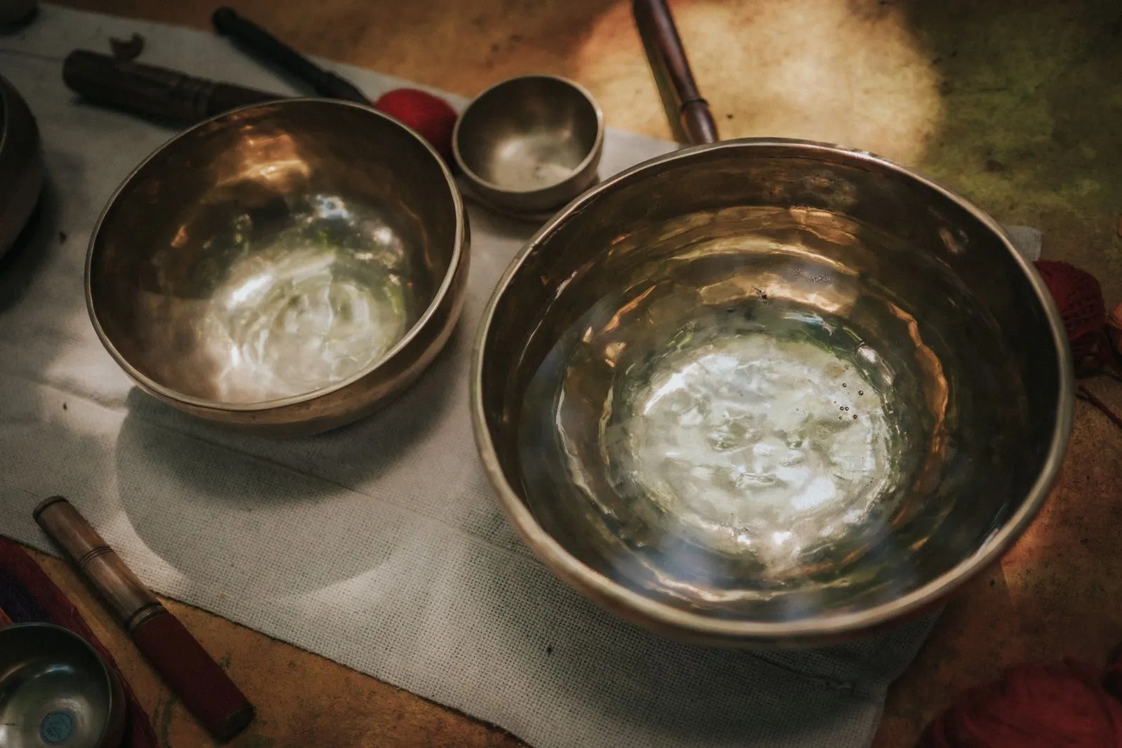 Two brass singing bowls sit on cream linen, filled with water that reflects morning light. Wooden, Lunita Jungle Retreat