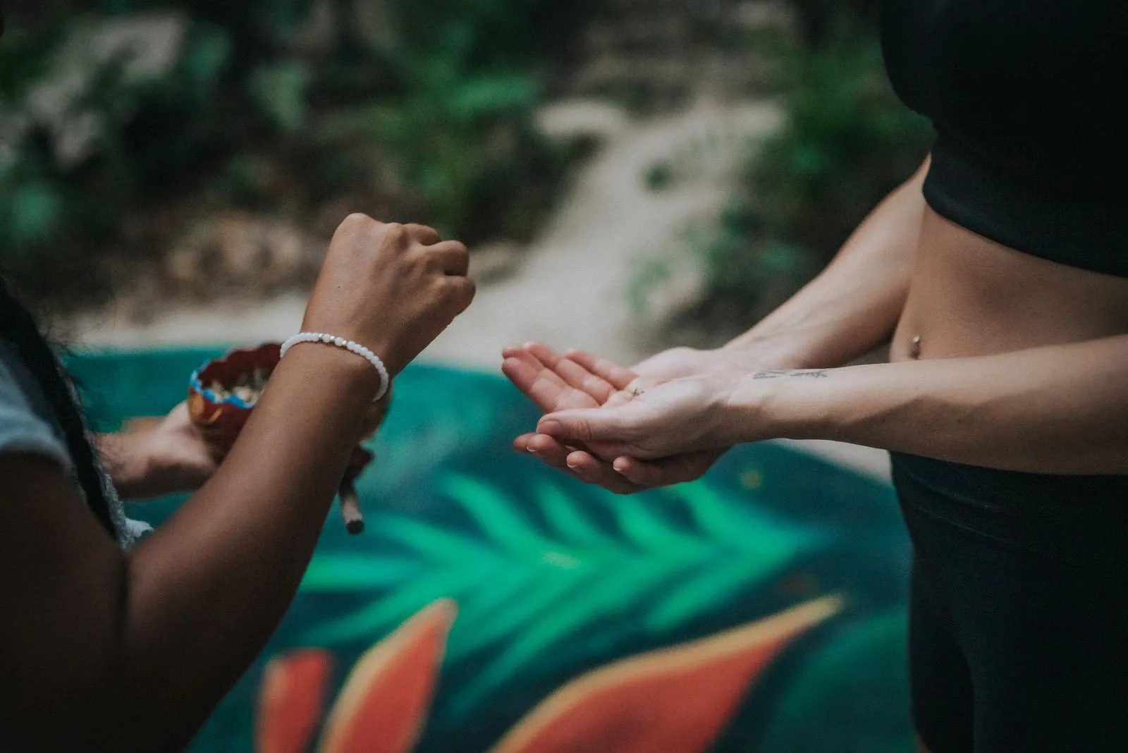Two people's hands meet in a gesture of connection above a teal fabric with tropical leaf print, Lunita Jungle Retreat
