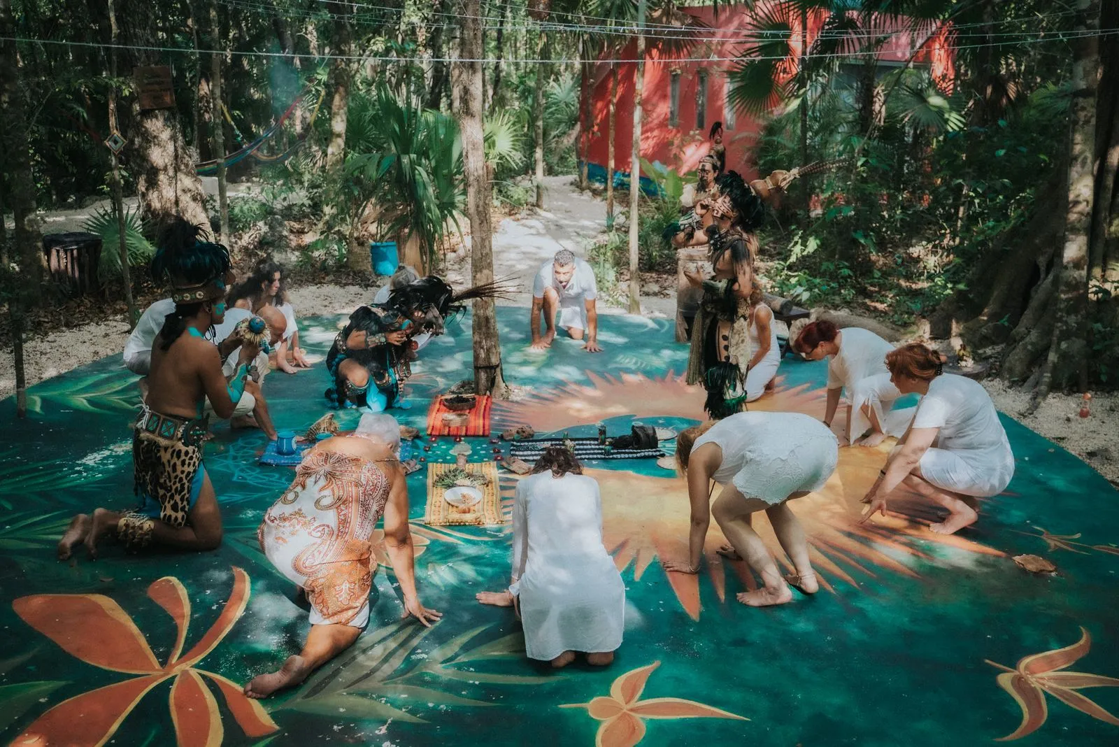 Twelve people in white and earth-toned clothing sit and crouch on a teal mat with painted ochre, Lunita Jungle Retreat