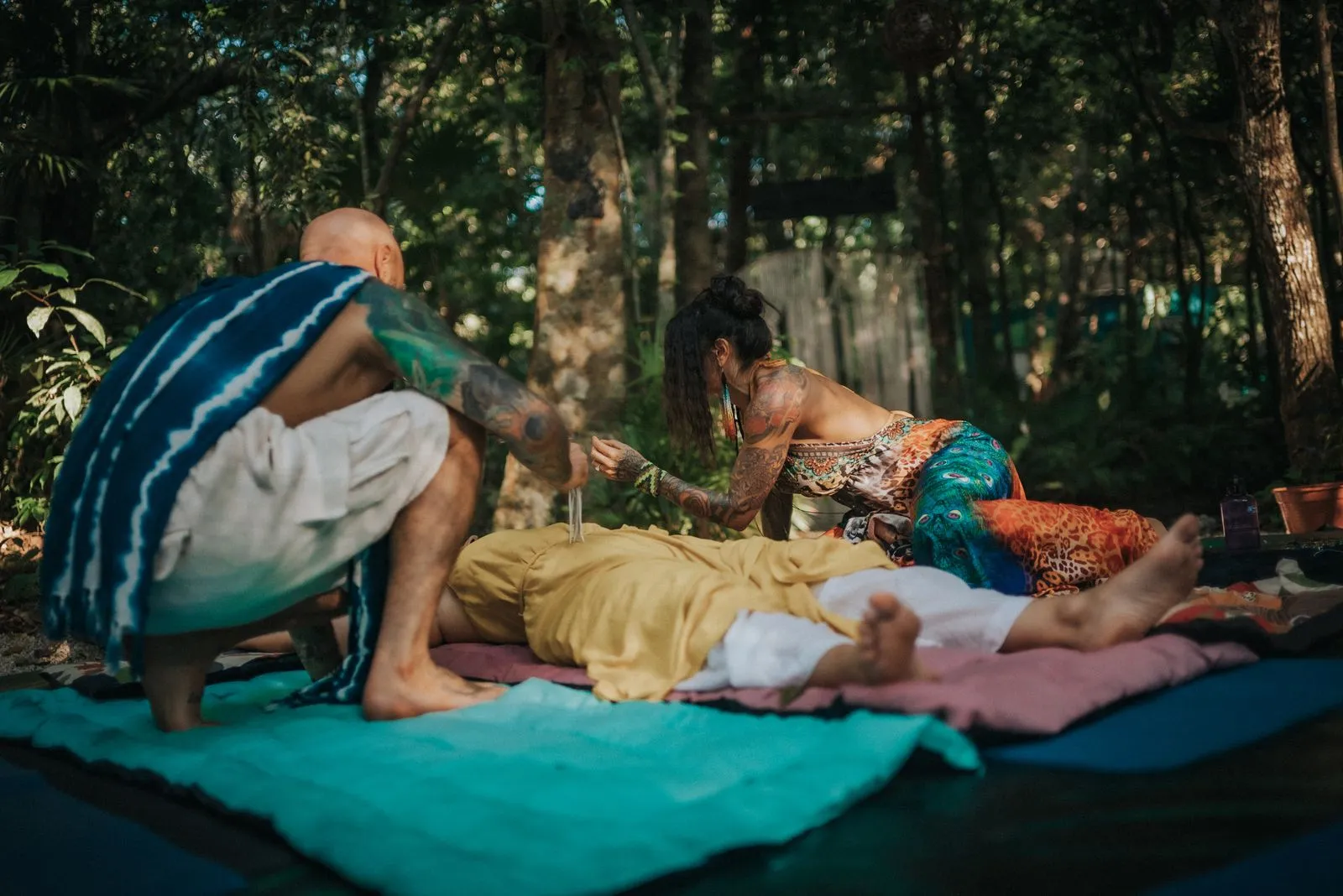 A facilitator in a blue and teal wrap works with a reclined participant on a turquoise yoga mat, Lunita Jungle Retreat