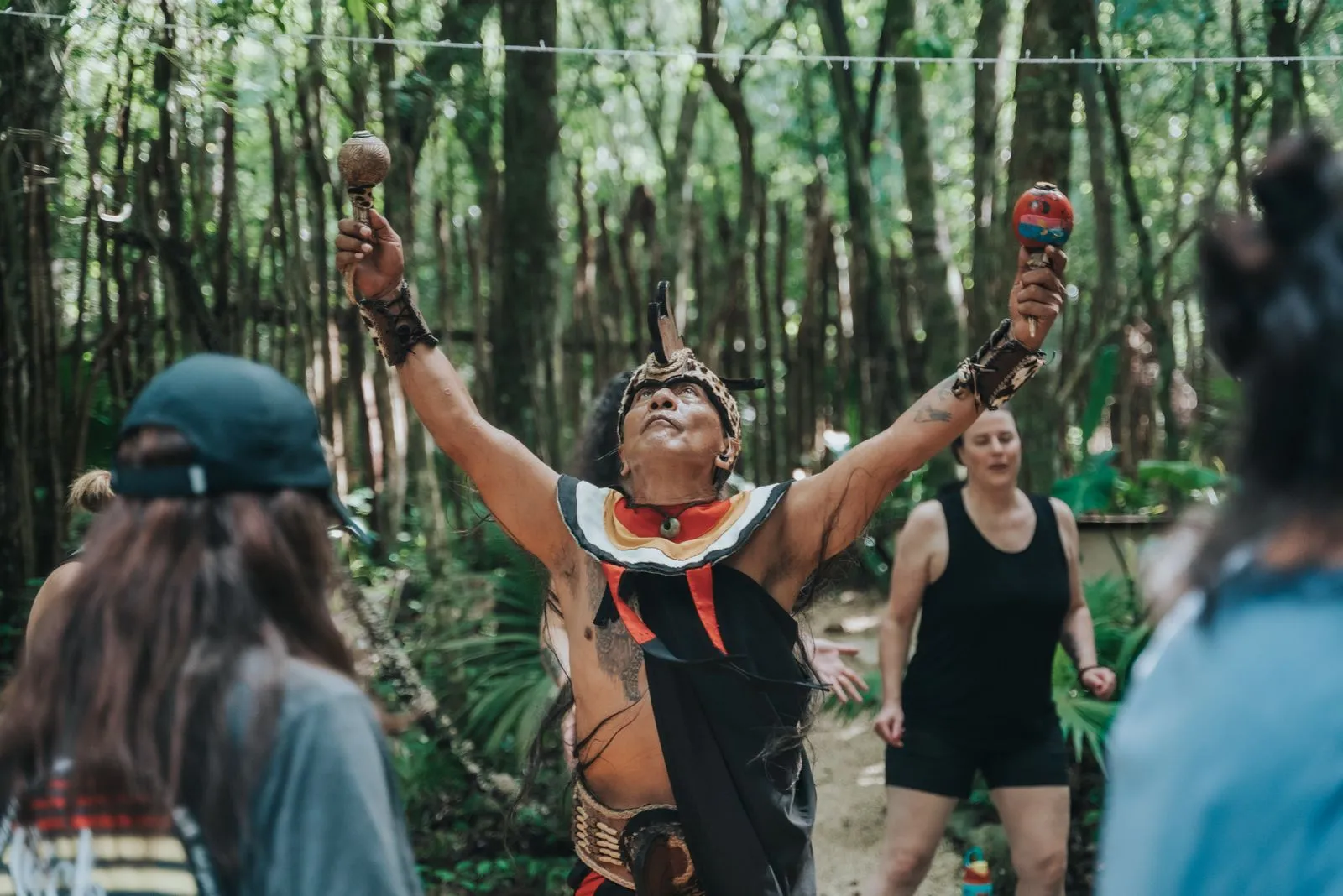 A shirtless man wearing indigenous Mayan regalia, red and white collar, black pants, beaded belt, Lunita Jungle Retreat