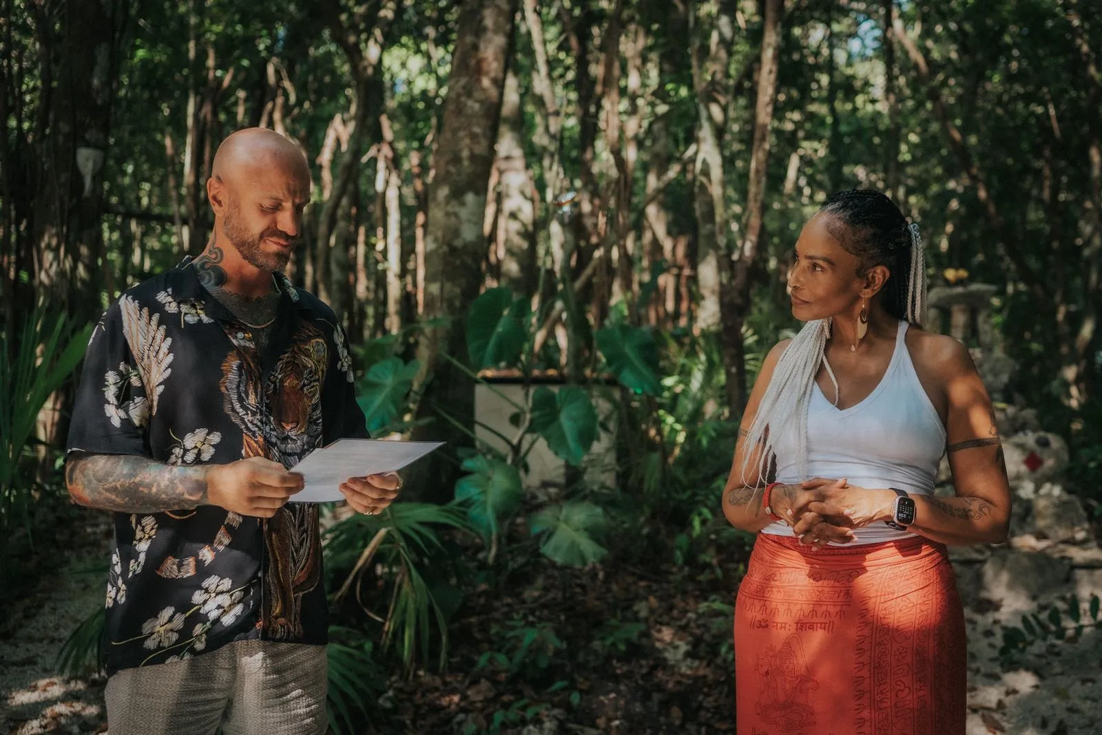 Two adults stand on a jungle path dappled with sunlight filtering through tall palms and dense green, Lunita Jungle Retreat
