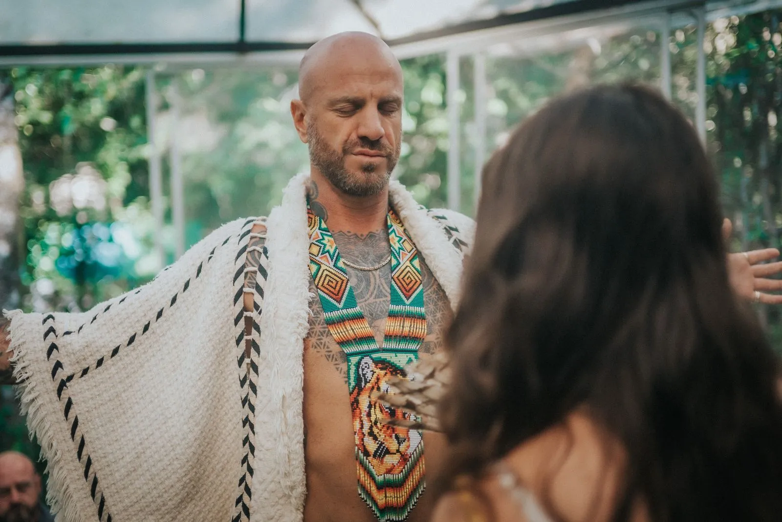 A man with a shaved head and beard, wearing a geometric-patterned woven vest in teal and orange, Lunita Jungle Retreat