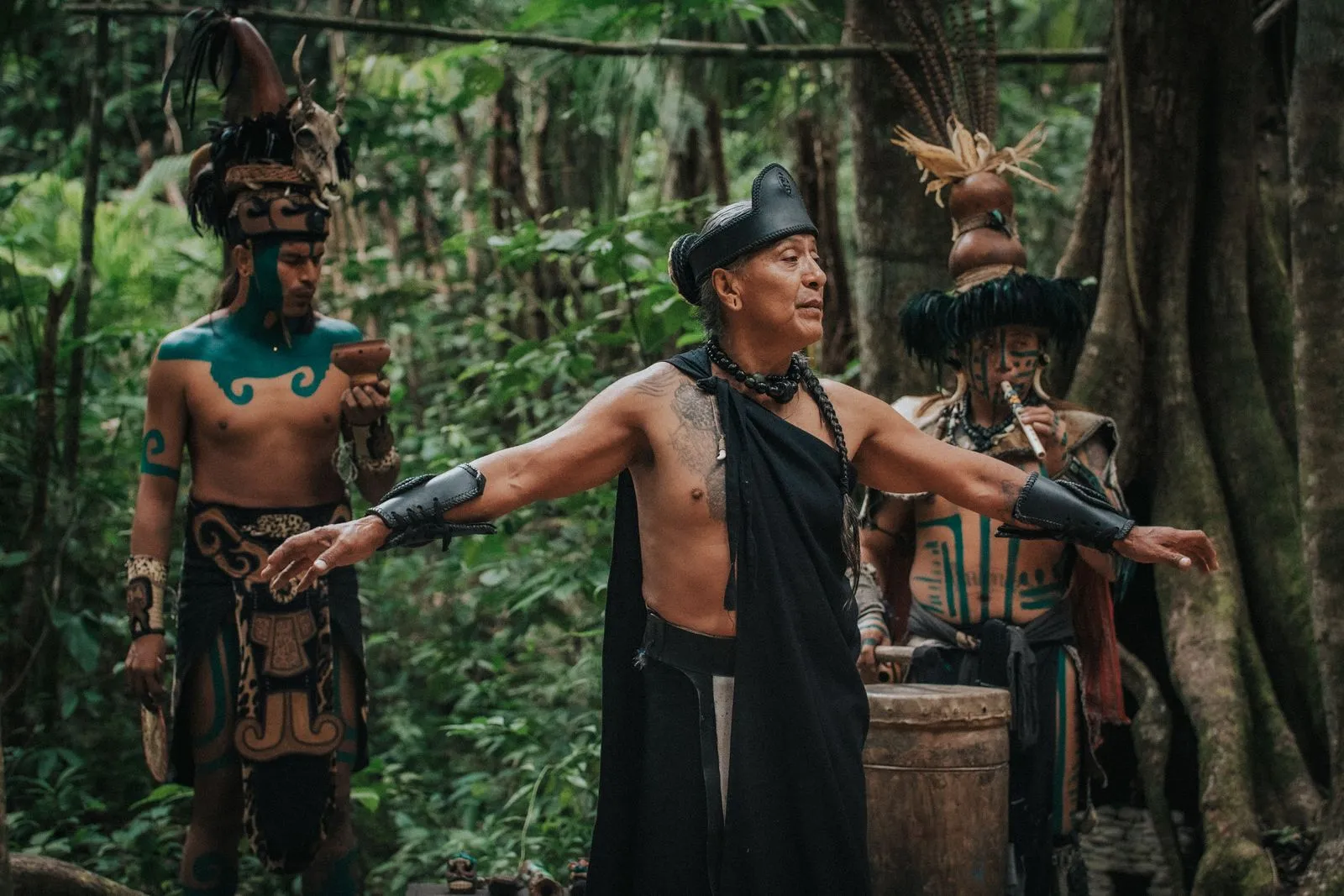 Three performers in indigenous Mayan ceremonial dress stand deep in jungle with dense green canopy, Lunita Jungle Retreat