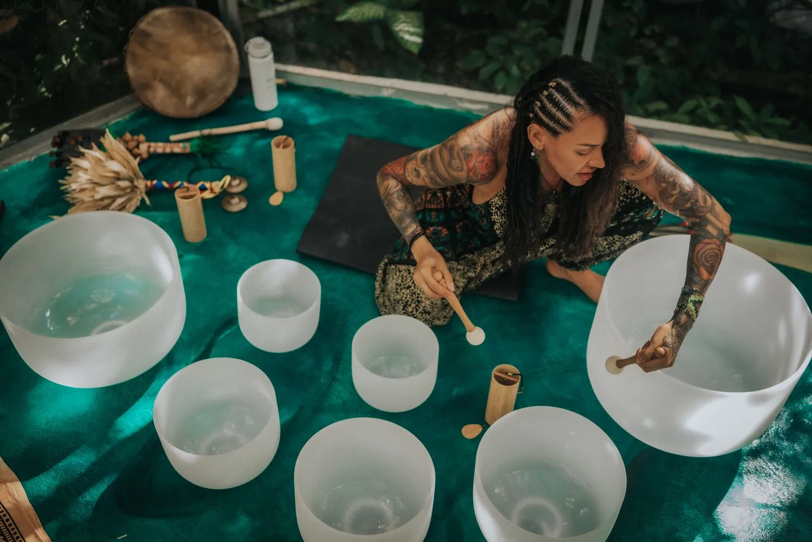A facilitator with braided hair and full-sleeve tattoos arranges singing bowls filled with water, Lunita Jungle Retreat