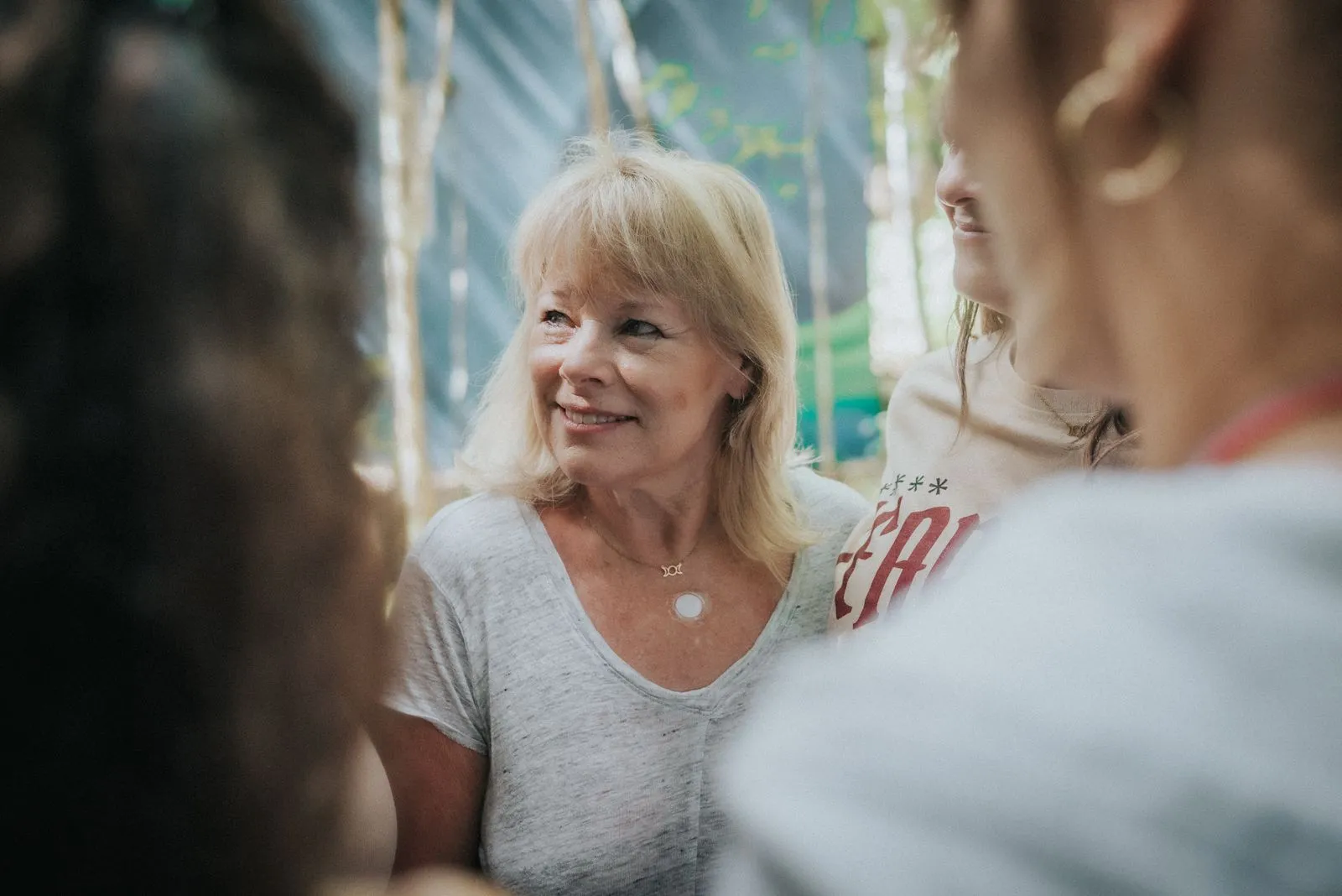 A woman with blonde hair in a light gray v-neck shirt smiles warmly while seated in conversation, Lunita Jungle Retreat