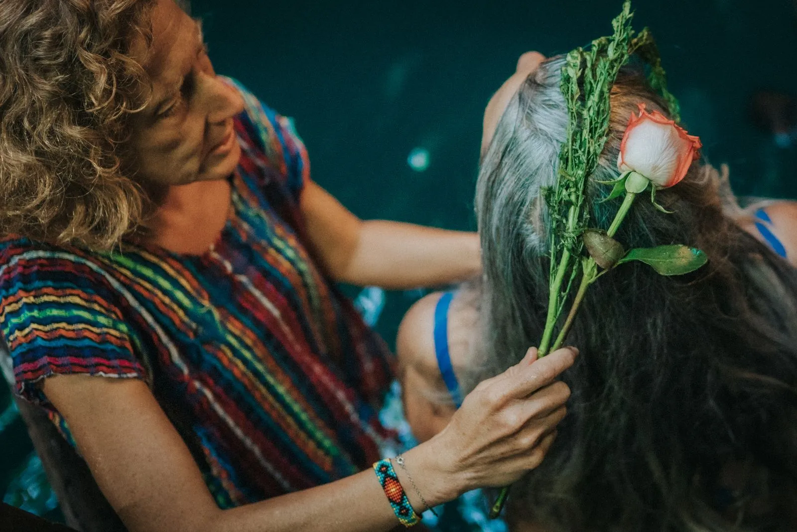 A person in a colorful striped shirt places a fresh red flower and green leaves into another person's, Lunita Jungle Retreat
