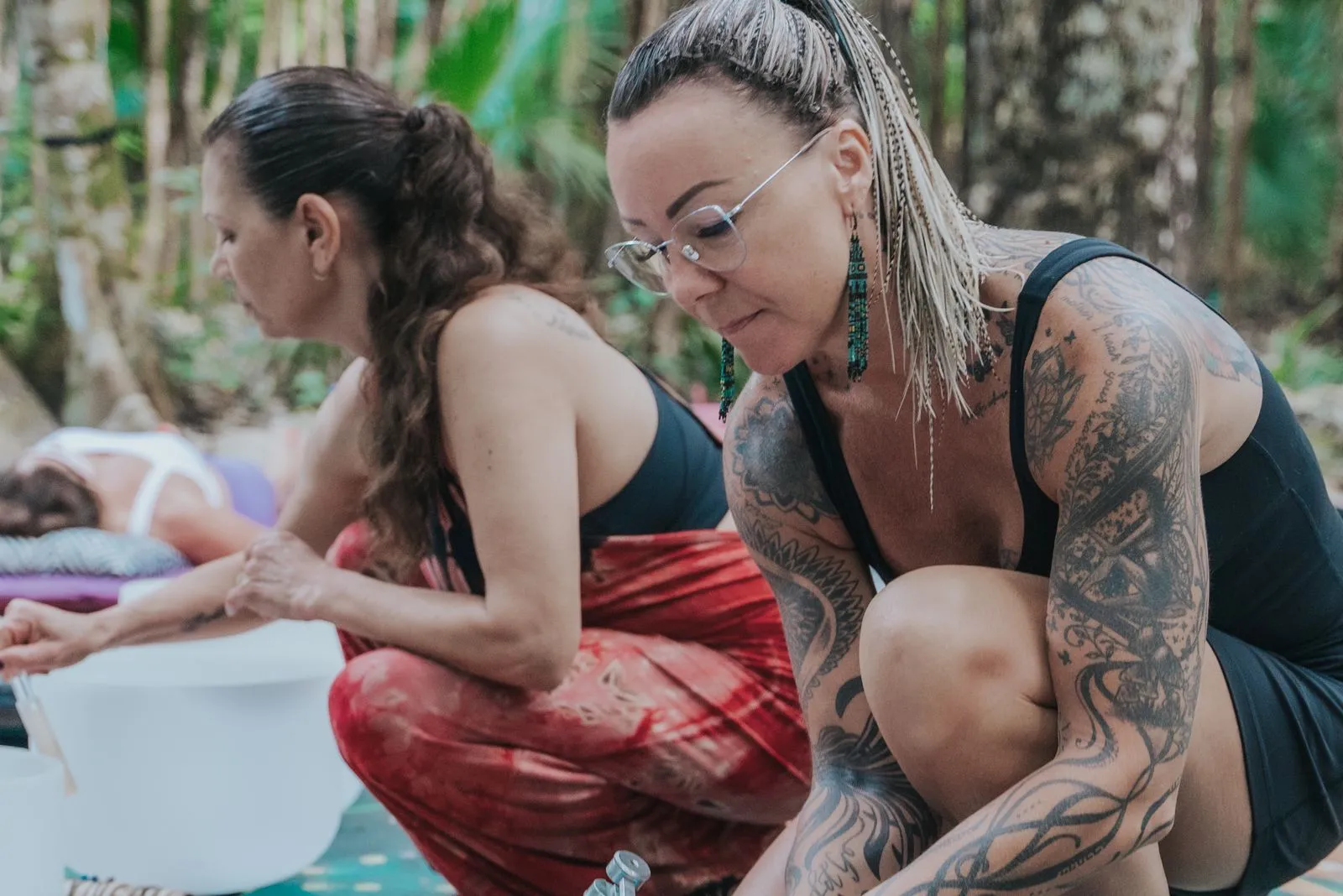 Three people seated on mats in dappled jungle shade, holding white ceramic vessels in a circle, Lunita Jungle Retreat
