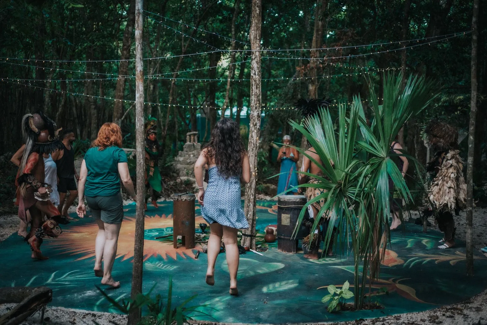 Twelve people move across a turquoise-painted jungle floor beneath strings of white lights strung, Lunita Jungle Retreat