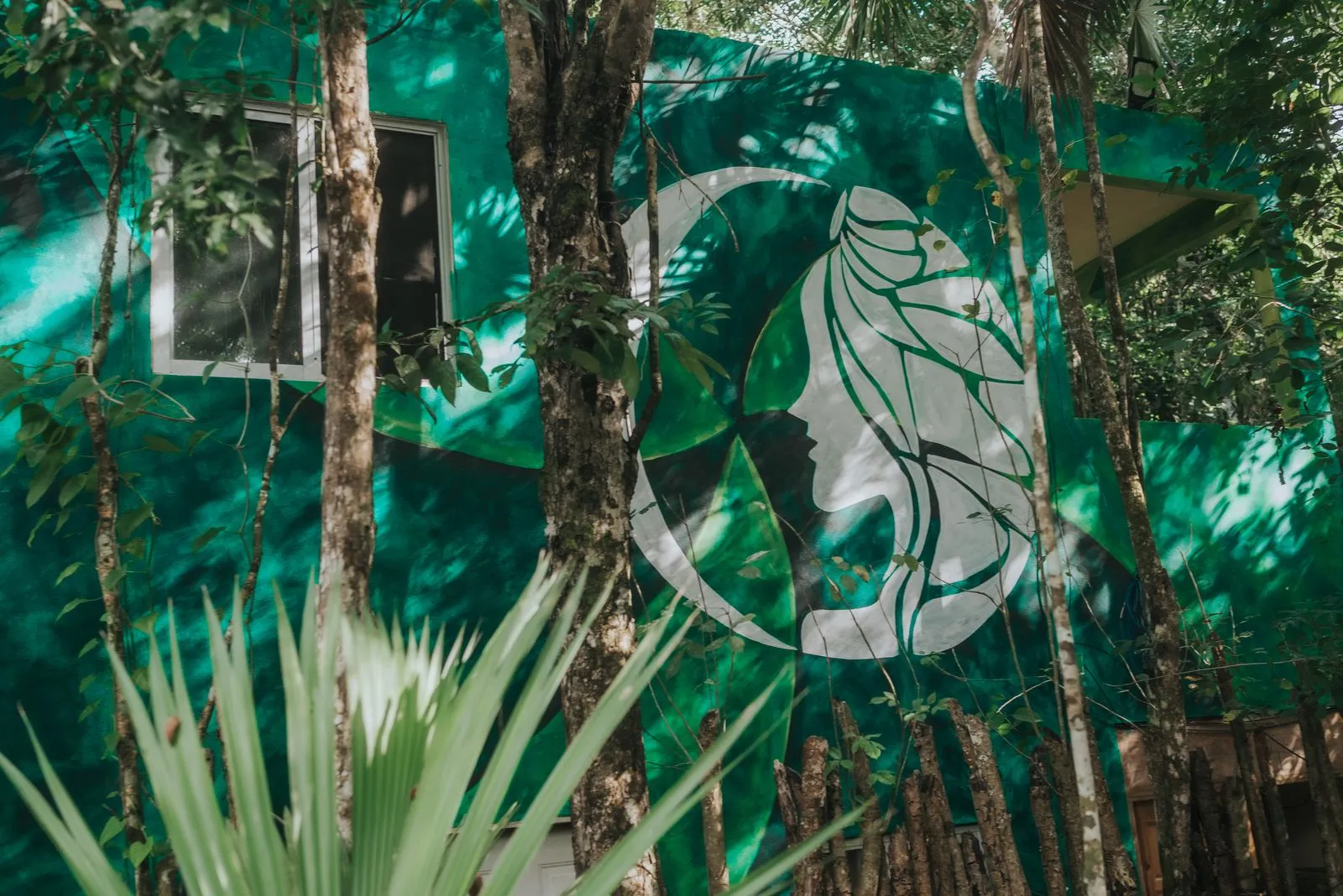 Bright turquoise building wall with a large white and teal mural of a profile face framed by organic, Lunita Jungle Retreat