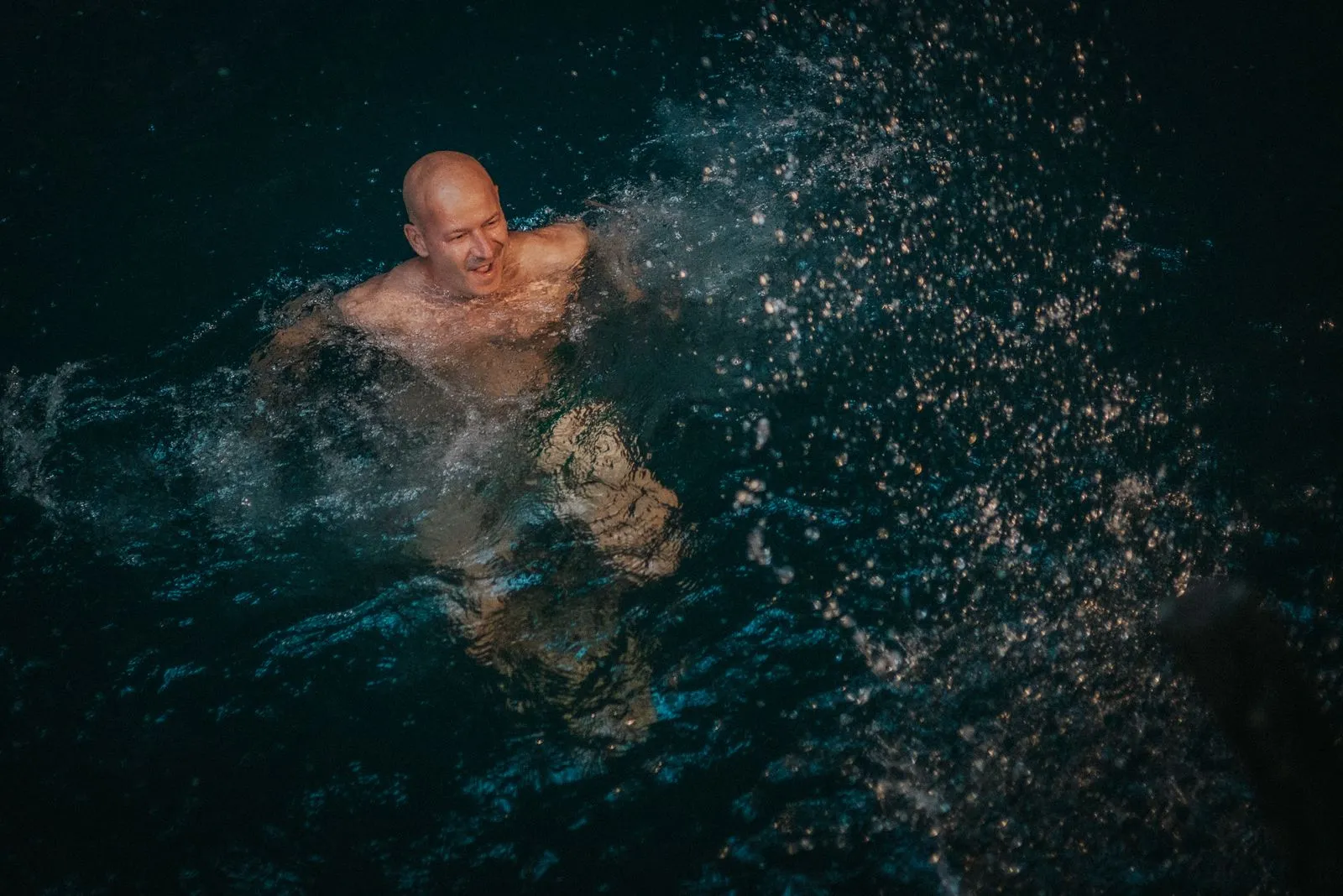 A man swims in deep teal cenote water, his face above the surface, Lunita Jungle Retreat