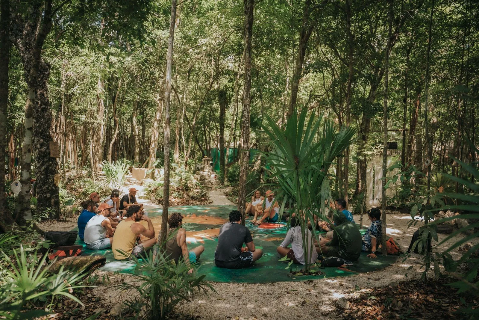 About 15 people sit in loose circles on teal and orange mats among tall hardwood trees, Lunita Jungle Retreat