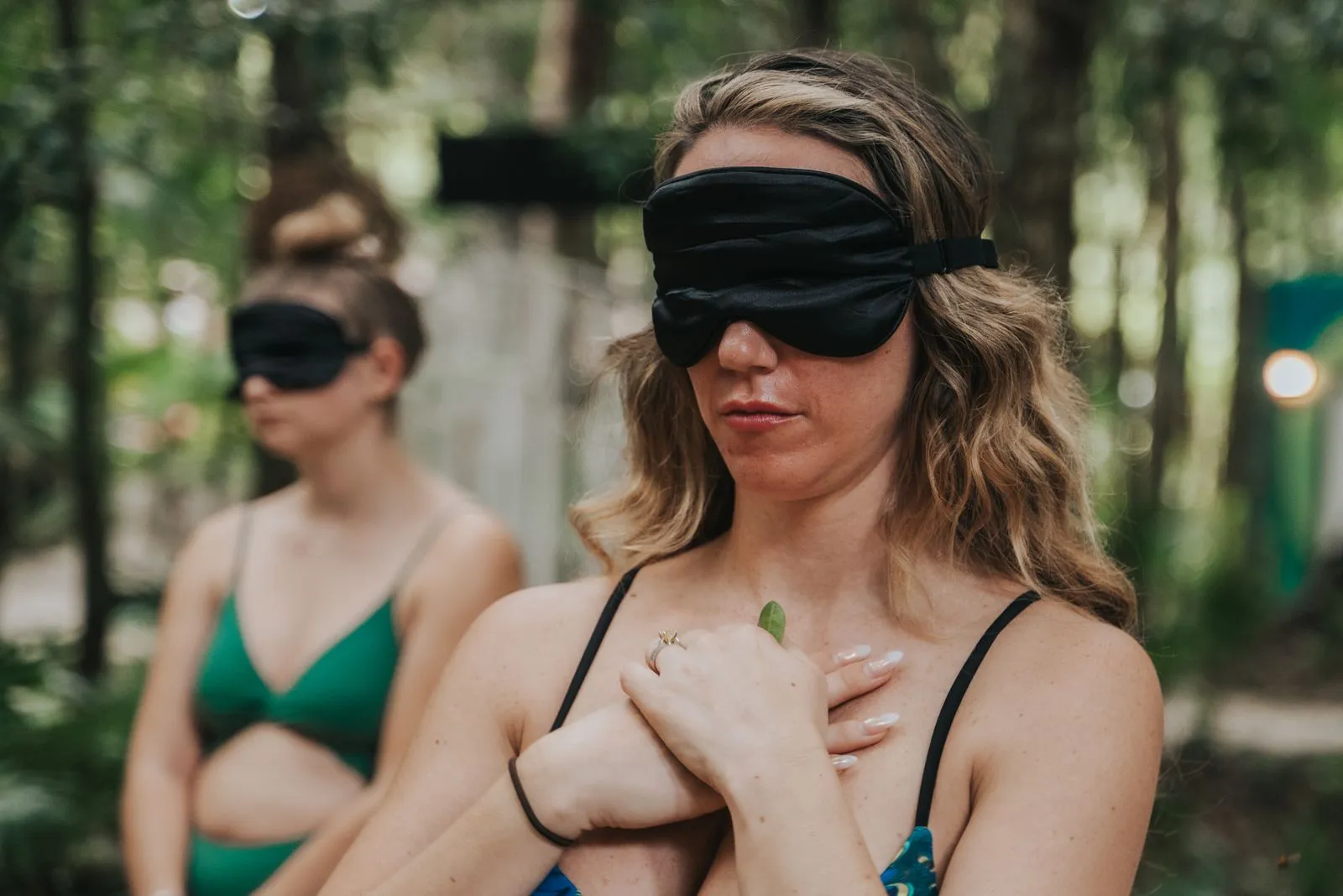 Two women wearing black silk eye masks stand in dappled jungle light, Lunita Jungle Retreat