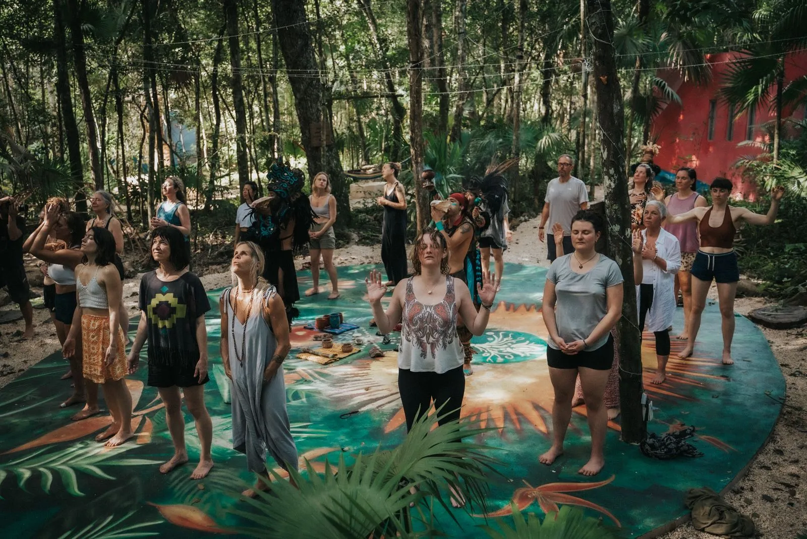 Twenty-five people stand barefoot on colorful patterned mats in a jungle clearing, Lunita Jungle Retreat