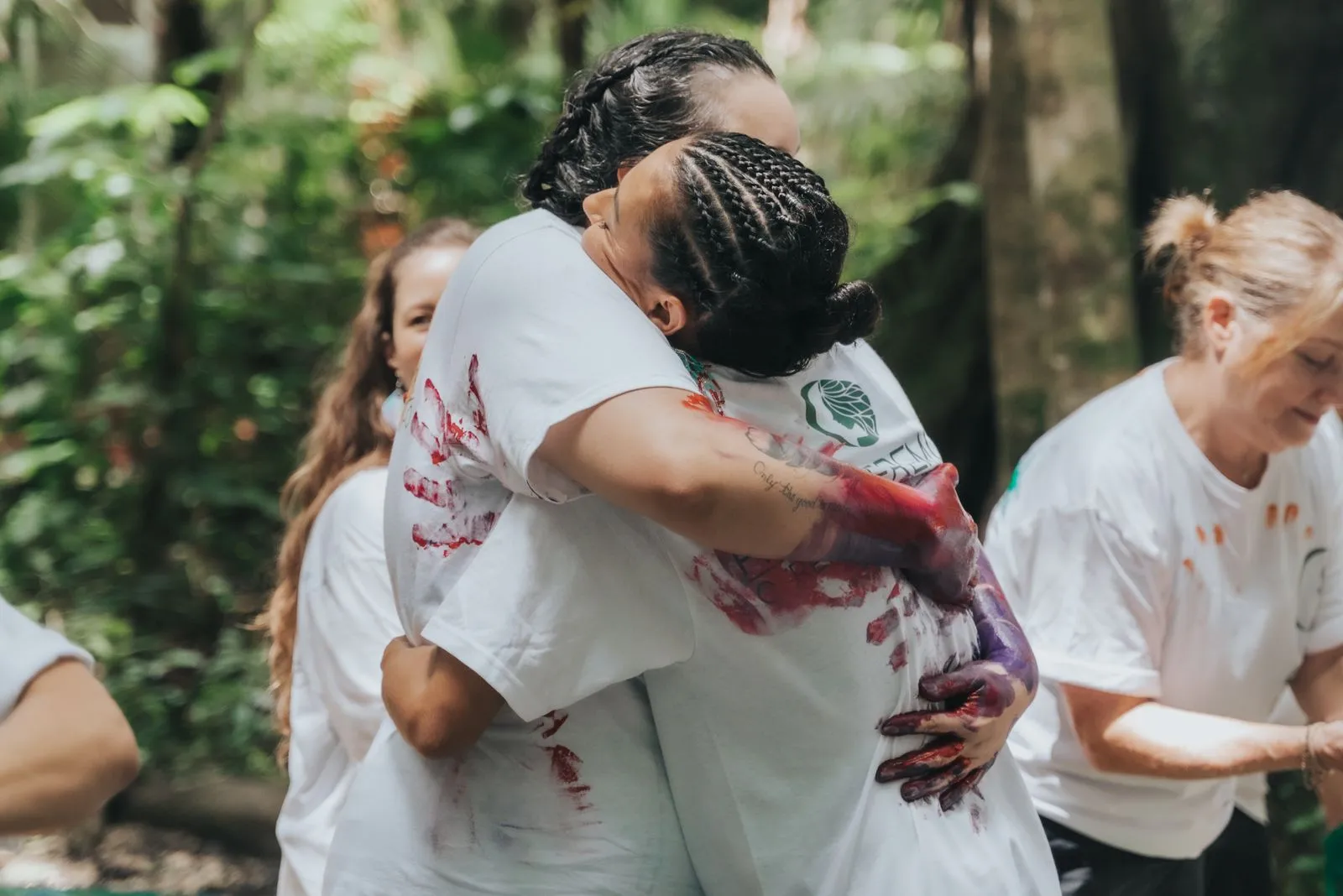 Two people embrace in the jungle, their white t-shirts stained with deep red and purple plant matter, Lunita Jungle Retreat