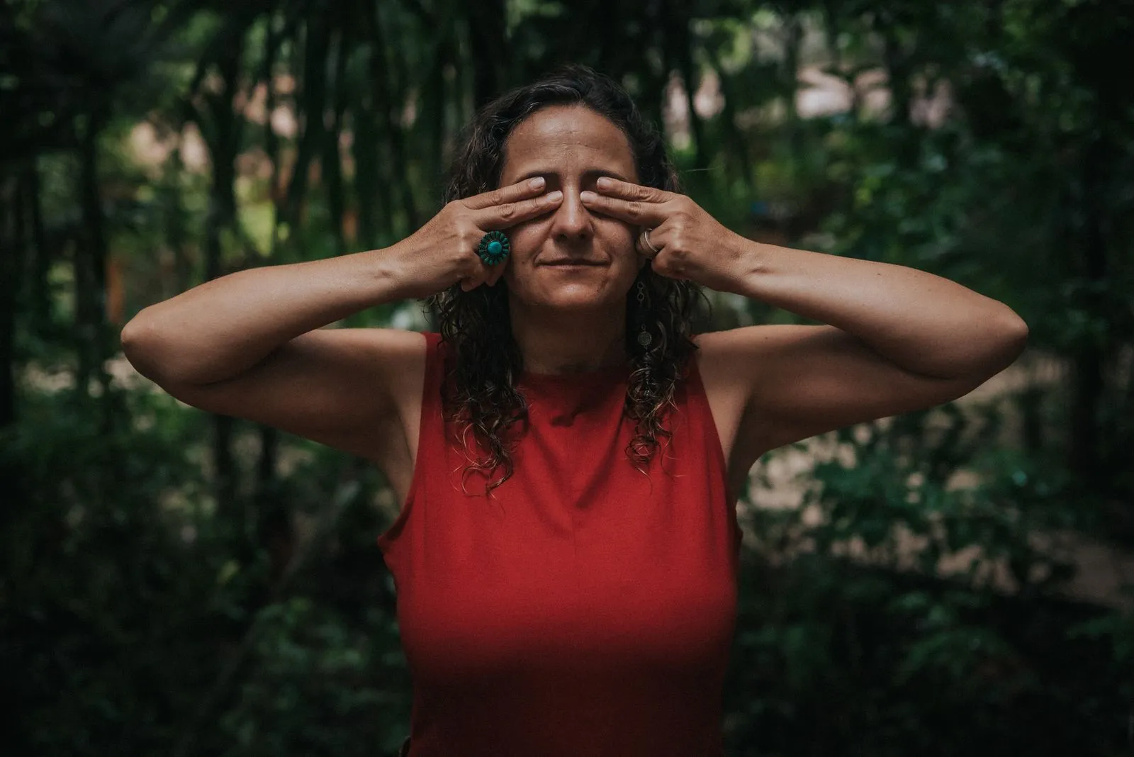 Woman with long dark curly hair and turquoise ring covers her eyes with both hands in a jungle path, Lunita Jungle Retreat
