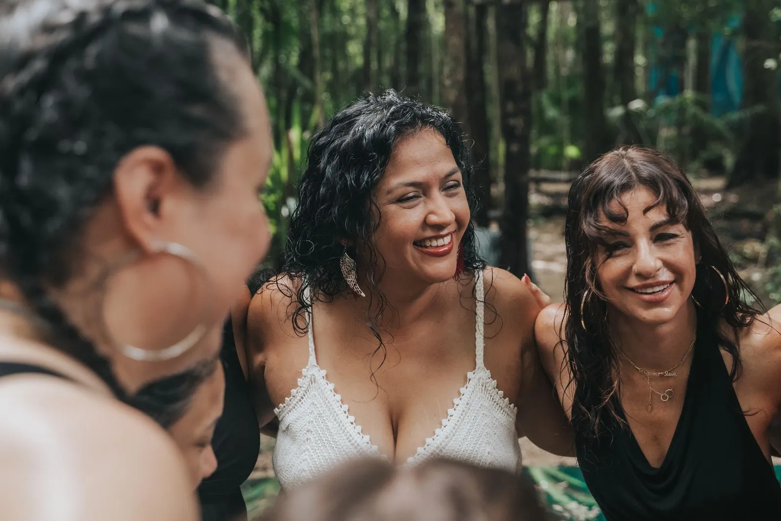 Four women laugh together on a jungle path, dappled light filtering through tall palms and vines. Two, Lunita Jungle Retreat
