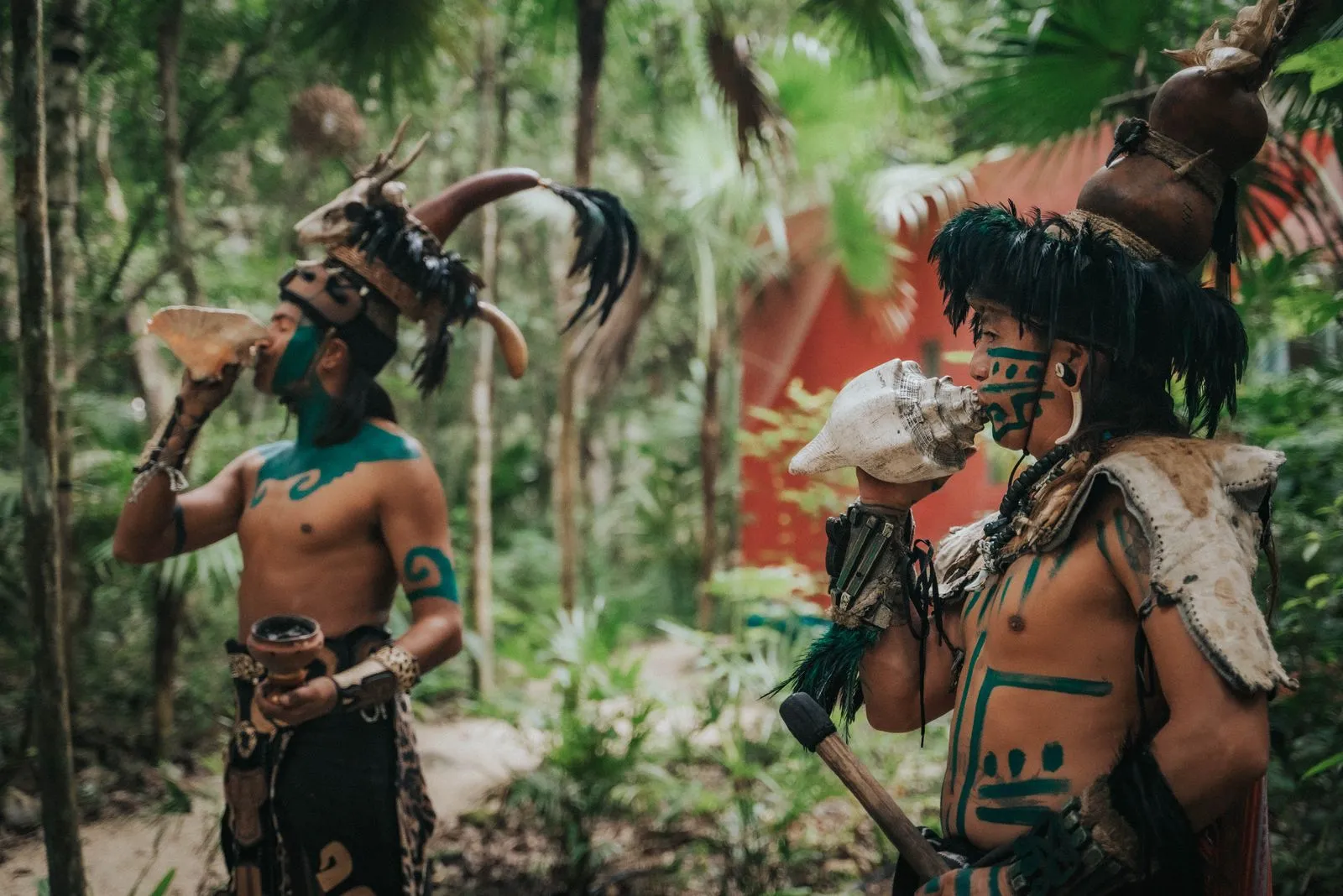 Two men in traditional Maya body paint and feathered headdresses hold ritual objects, Lunita Jungle Retreat