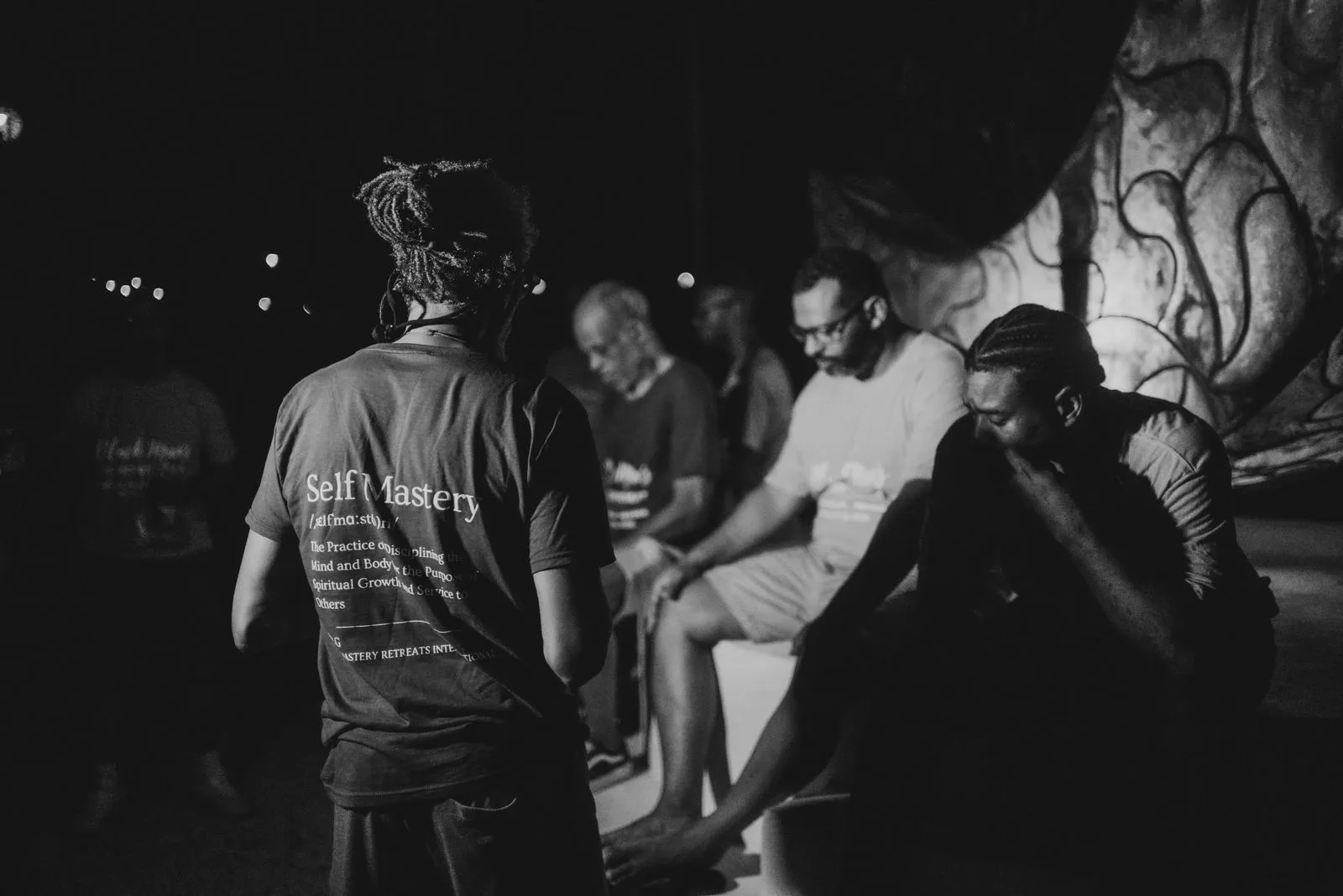Night ceremony under a palapa with string lights, a facilitator in a 'Self Mastery' shirt facing, Lunita Jungle Retreat