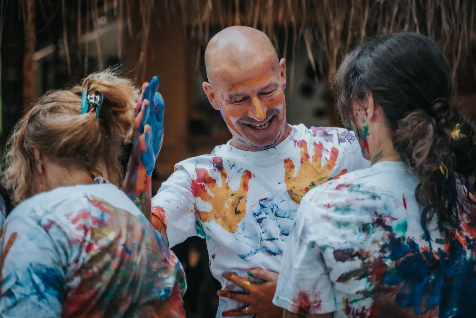 Three people in paint-stained white shirts stand in a circle under a palapa, Lunita Jungle Retreat