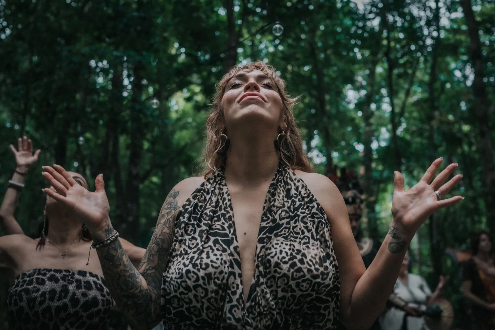 A woman with wavy hair and visible tattoos on her arms stands in dappled jungle light, Lunita Jungle Retreat