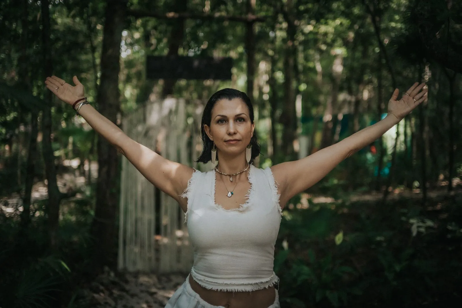 A woman in a white sleeveless top stands with arms raised in a jungle path, Lunita Jungle Retreat