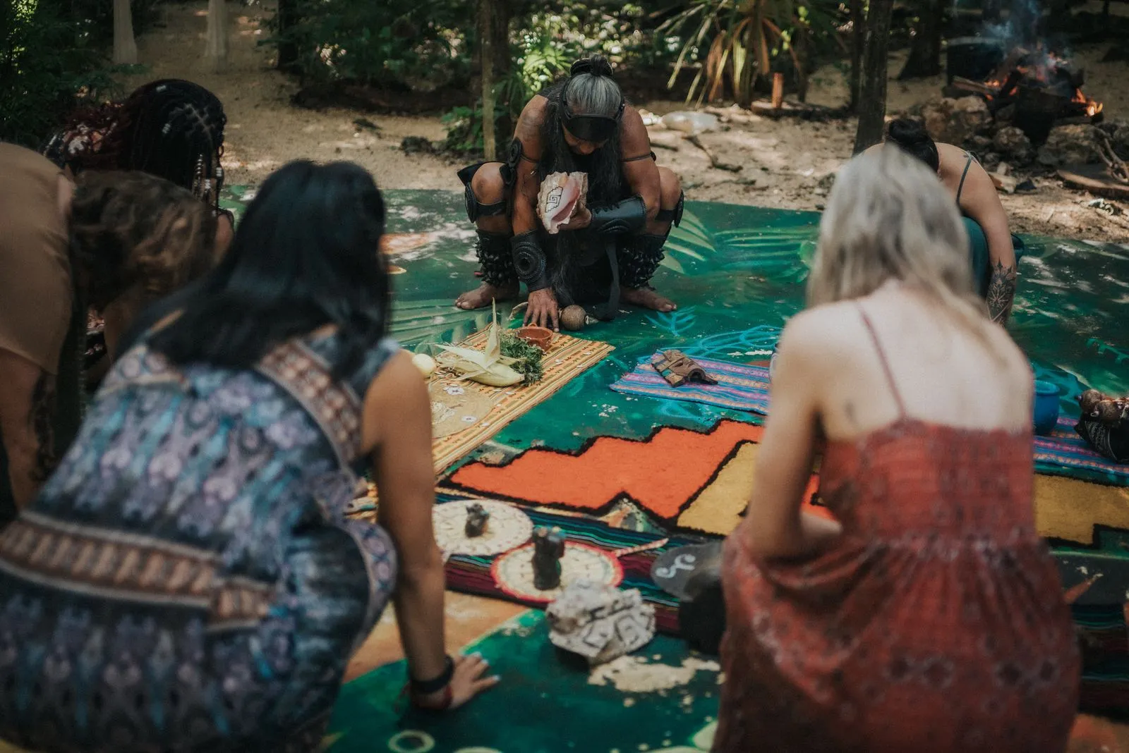 A facilitator in dark clothing crouches over a woven mat in the jungle, Lunita Jungle Retreat