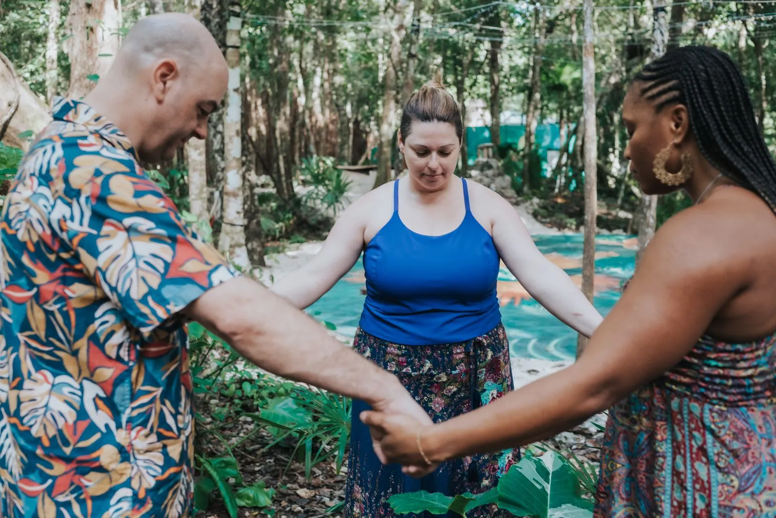 Three people stand in a circle holding hands on a teal-painted wooden platform surrounded by tall, Lunita Jungle Retreat