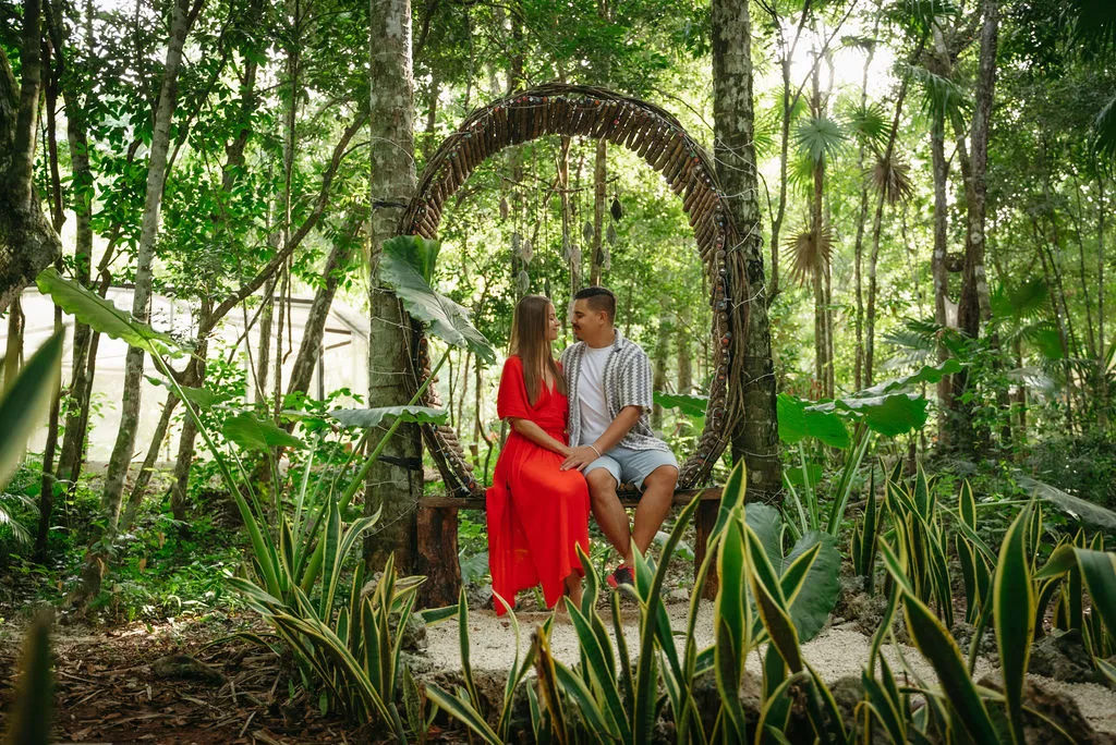 Couple in earthy tones seated on concrete pool deck with turquoise water and dense tropical canopy framing the shot. Intimate moment showcasing the retreat's lush garden setting an